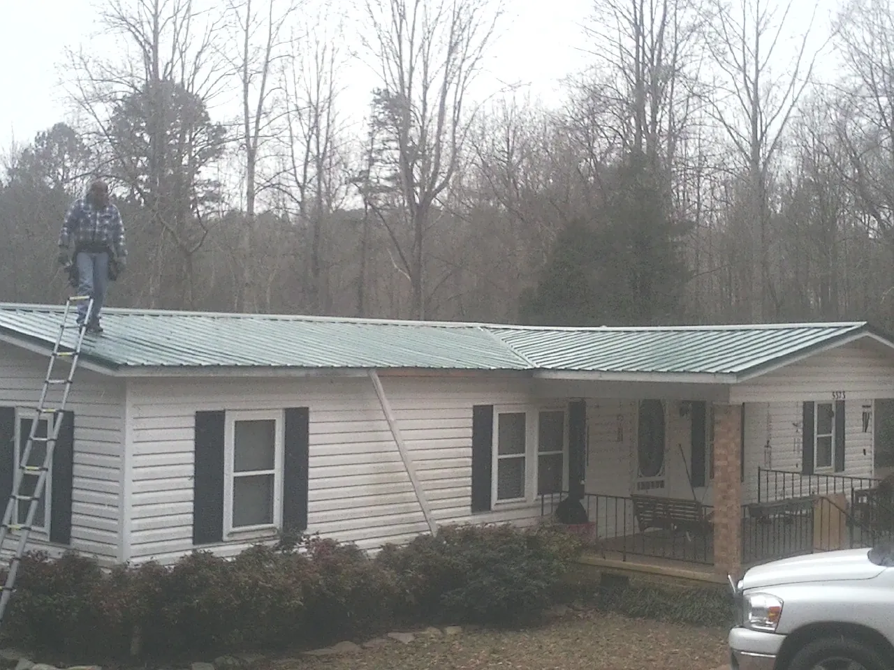 Worker on a ladder beside a new green metal roof on a ranch home in Hewitt