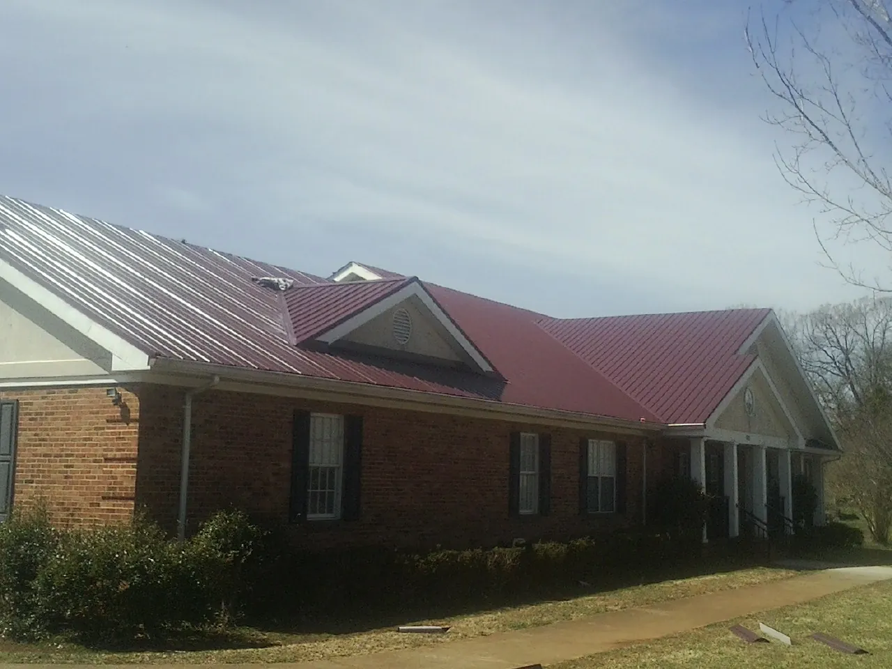 Red metal roof with gabled entries on a long brick building, from a Hail Damage Roof Repair job in Hewitt