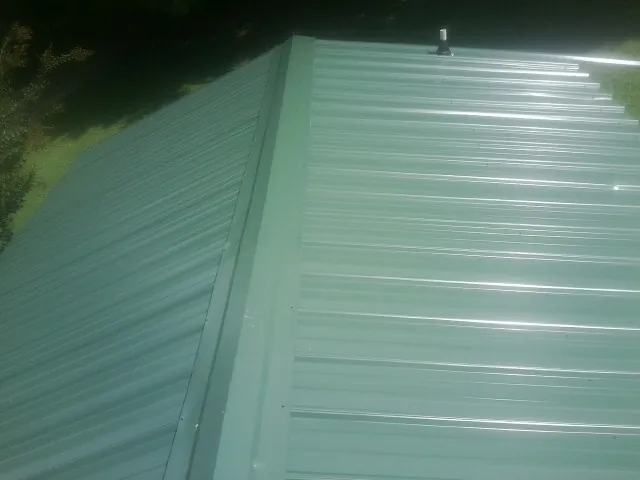 New green metal panels meeting at the ridge of a roof — Flat Roof Repair work by our crew in Hewitt