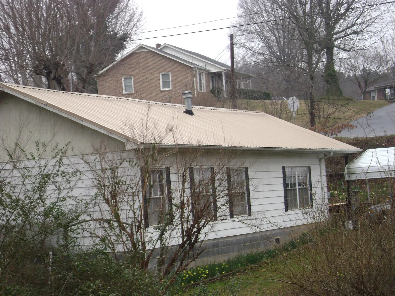 Tan metal roof on a white sided house set into a hillside — Commercial Roofing by Roofing Brothers in Hewitt
